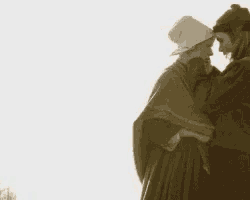 a man and a woman are hugging each other . the woman is wearing a white hat .