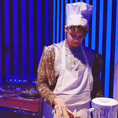 a man wearing a chef 's hat and apron is standing in front of a blender