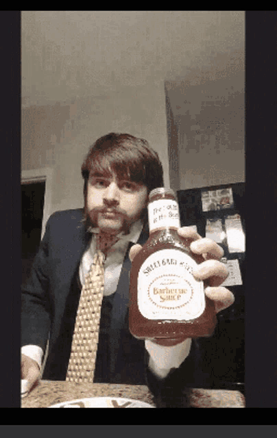 a man in a suit and tie holds up a bottle of sweet baby ray 's barbecue sauce