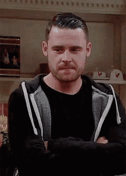 a man with a beard is standing in a living room with his arms crossed and looking at the camera .