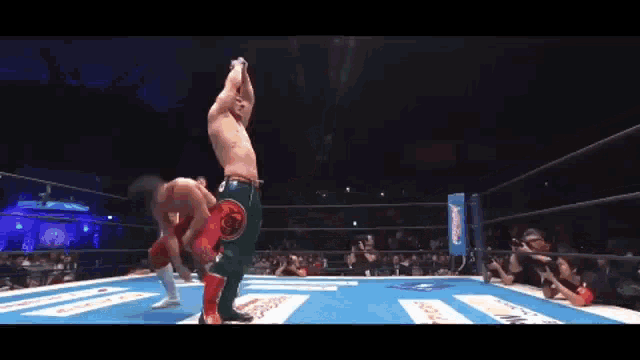 two men are wrestling in a ring with a crowd watching . one of the men is wearing a green outfit .