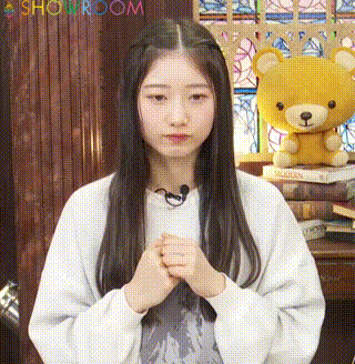 a girl with long hair is standing in front of a teddy bear and books .