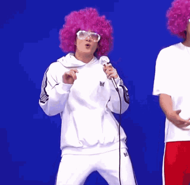 a man in a pink afro wig is singing into a microphone .