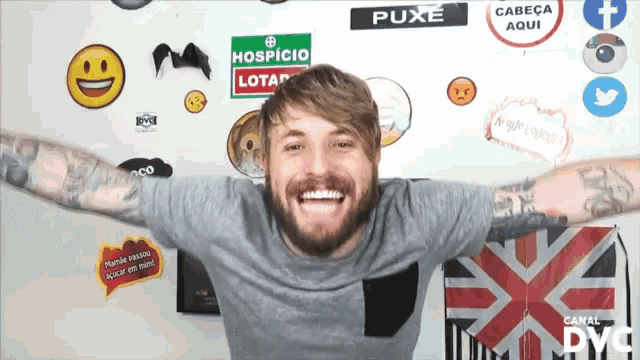 a man with his arms outstretched is smiling in front of a wall with stickers on it including one that says puxe