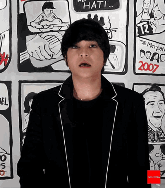 a man in a black jacket stands in front of a wall with drawings of people and the year 2007 on it