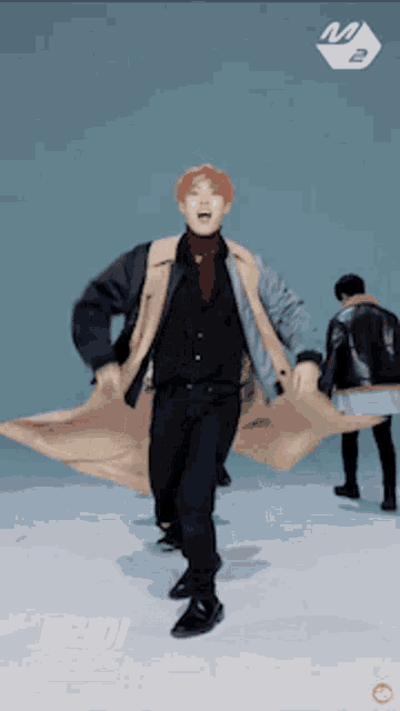 a man in a trench coat is dancing in front of a blue background with the letter m on it