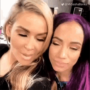 two women with purple hair are standing next to each other .