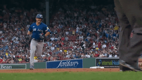 a baseball player wearing a blue jays uniform is running towards home plate