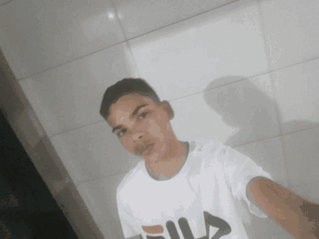 a young man wearing a white fila shirt taking a selfie