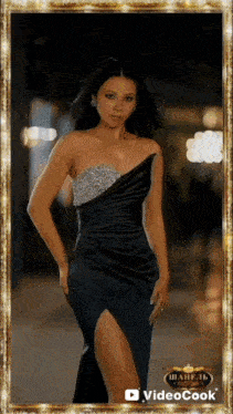 a woman in a black dress with a high slit is standing in front of a gold frame .
