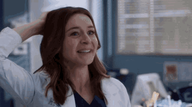 a woman in a lab coat is smiling while holding her hair .