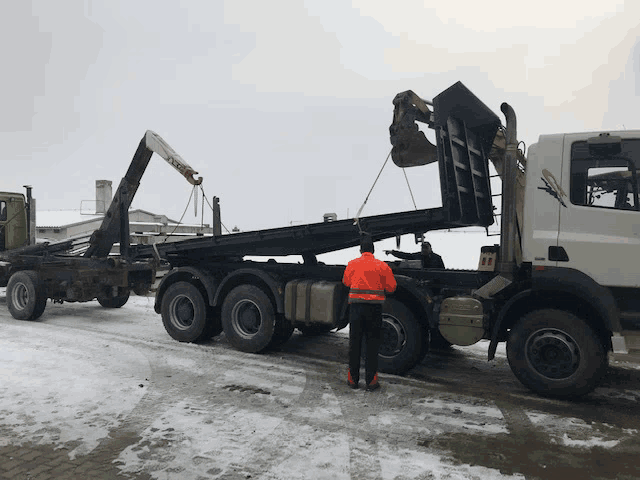 a man in an orange jacket is standing next to a dump truck with the number 11 on it