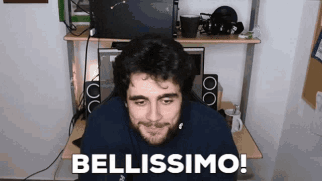 a man with a beard is sitting at a desk with the words bellissimo written on it