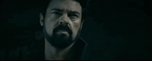 a man with a beard and mustache is looking at the camera in the dark .