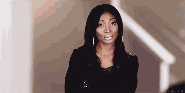 a woman wearing hoop earrings and a black top is standing in front of stairs .