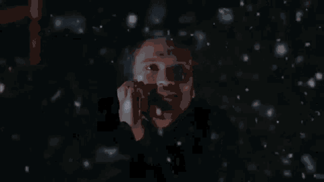 a close up of a person 's face in the dark with snow falling .
