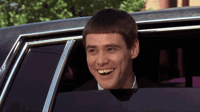 a man in a suit is smiling while sitting in a car
