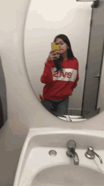 a woman in a red levi 's shirt takes a picture of herself in a bathroom mirror