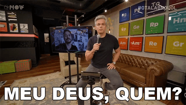a man sitting on a couch holding a microphone with the words meu deus quem written in front of him