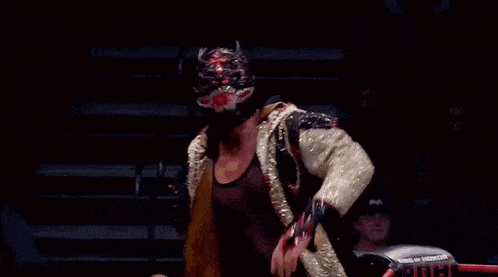 a wrestler wearing a mask and a gold jacket adjusts his mask