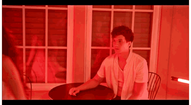 a man in a white shirt is sitting at a table in front of a red light .