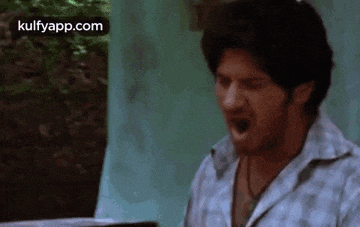 a man is screaming with his mouth open while sitting in front of a window .