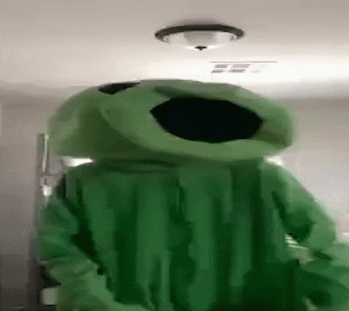 a person in a green alien costume is standing in a room with a ceiling light .