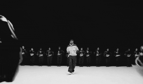 a black and white photo of a man standing in front of a group of people dancing .