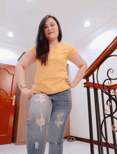 a woman wearing ripped jeans and a yellow shirt stands in front of a railing