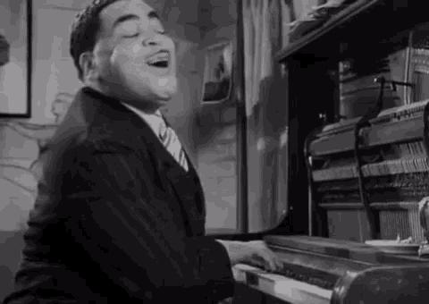 a man in a suit and tie is singing while playing a piano in a black and white photo .