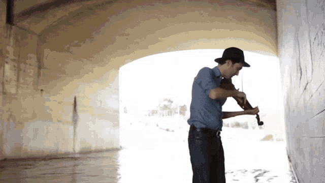 a man in a hat plays a violin in a tunnel