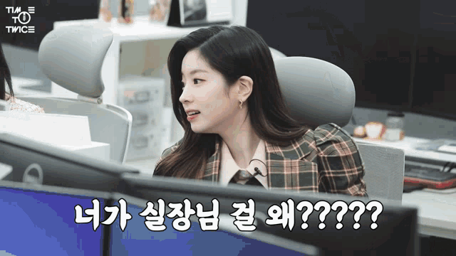 a woman in a plaid jacket sits in front of a computer screen with twice written on the bottom right corner
