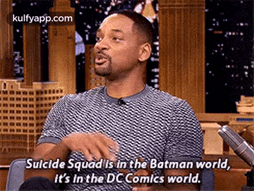 a man is sitting in front of a microphone and talking about suicide squad .