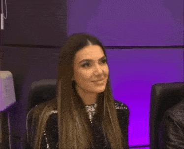 a woman in a black dress is sitting in front of a purple wall and clapping her hands .