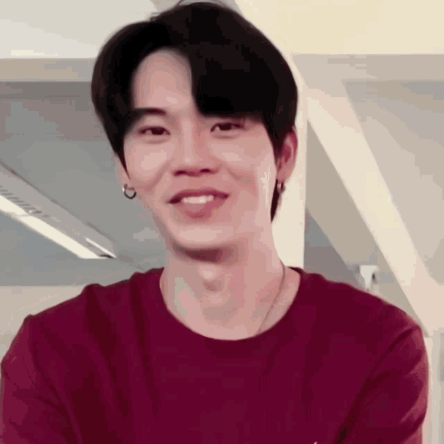a young man wearing a red t-shirt and earrings smiles for the camera