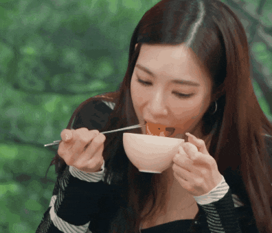a woman eating a bowl of food with chopsticks