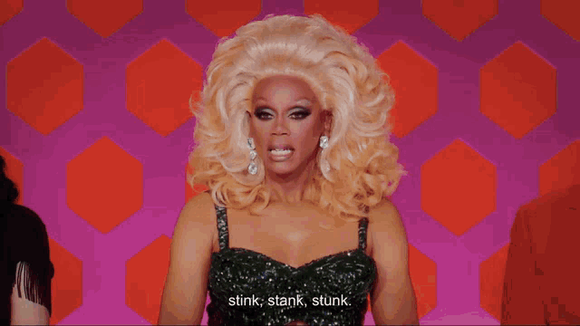 a drag queen says " stink stank stunk " in front of a colorful background