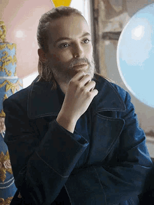 a man with long hair and a beard is wearing a blue coat