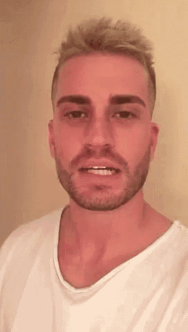 a man with a beard and blonde hair is wearing a white t-shirt and smiling .