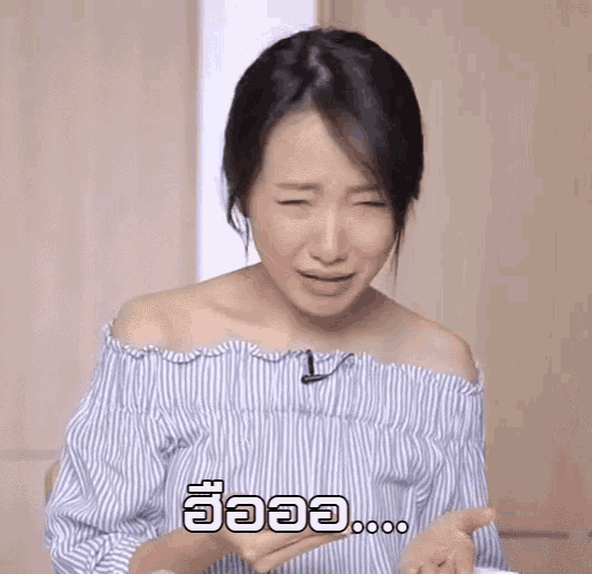 a woman in a blue and white striped off the shoulder top is making a funny face while holding something in her hand