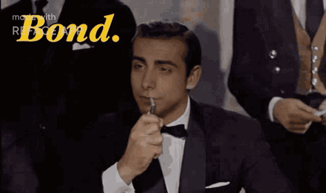 a man in a tuxedo is lighting a cigarette with the word bond in the background .