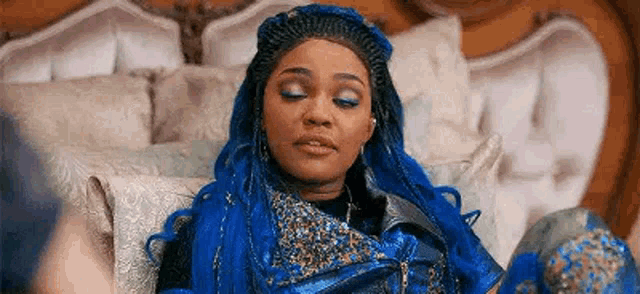 a woman with blue hair is sitting on a couch in a bedroom .