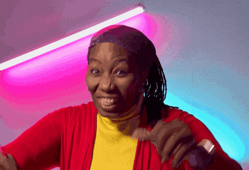 a woman wearing a red sweater and a yellow turtleneck is smiling and giving a thumbs up
