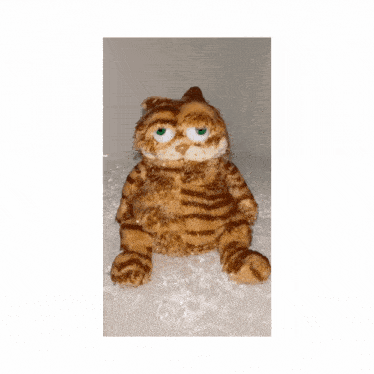 a stuffed garfield cat with green eyes is sitting in a pile of snow