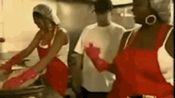 a woman in a red dress is dancing in a kitchen while a man looks on .
