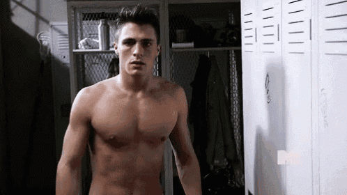 a shirtless man is standing in a locker room next to a row of white lockers .