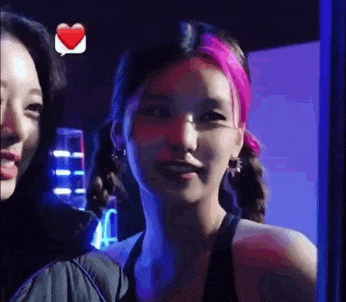 a woman with pink hair is standing next to another woman in a room .