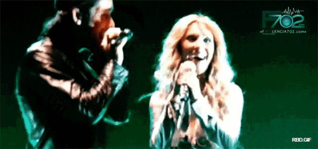 a man and a woman singing in front of a green background that says f702 on it