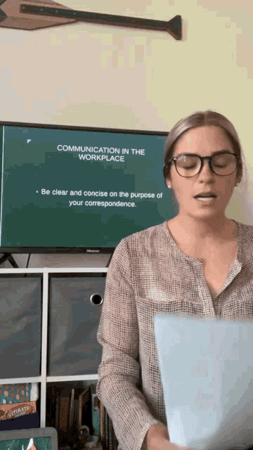 a woman is standing in front of a tv screen that says communication in the workplace