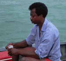 a man in a blue shirt is sitting on a red cooler in front of a body of water
